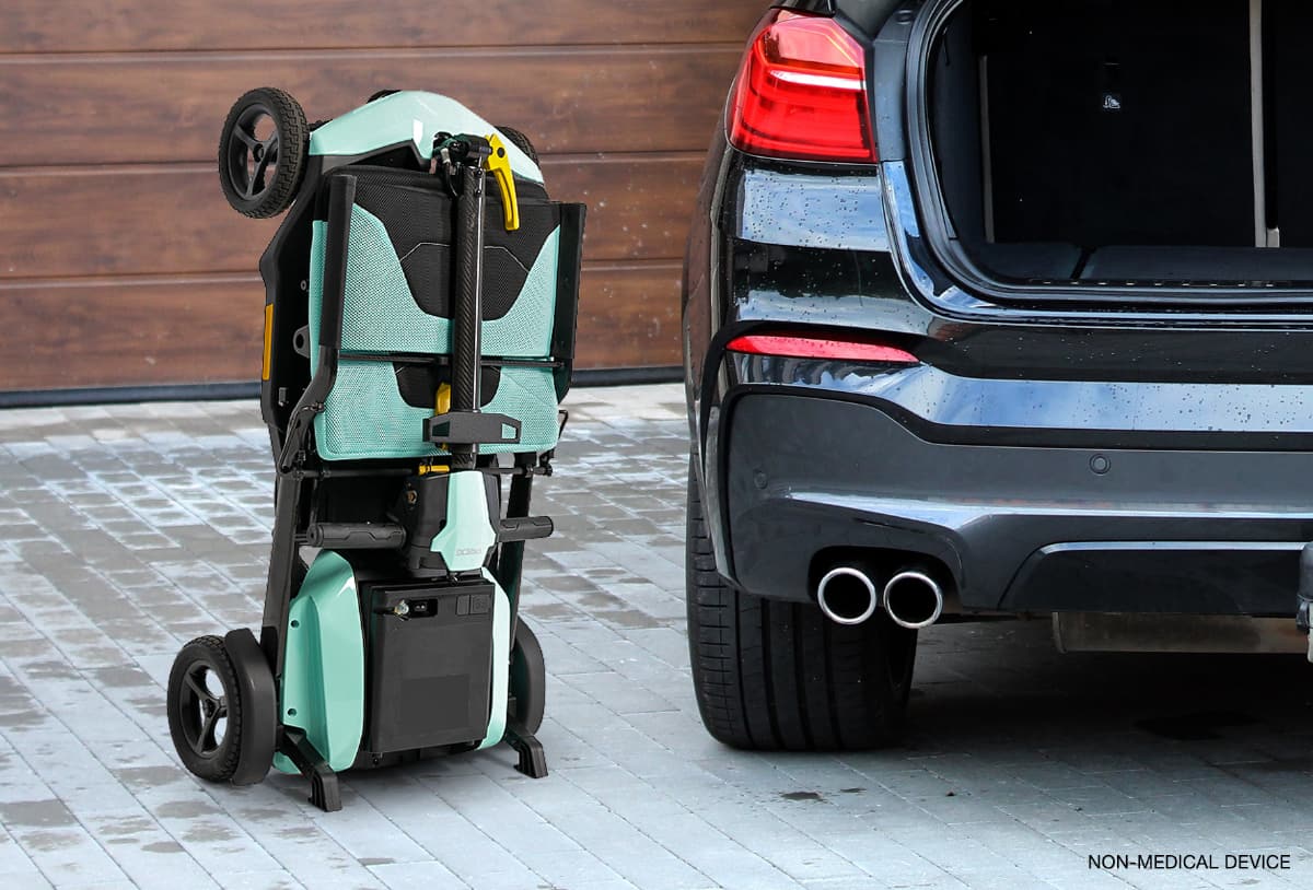 Pride Go Go Super Portable mobility scooter with sleek design in mint color folded and in standing position next to an open trunk of a car